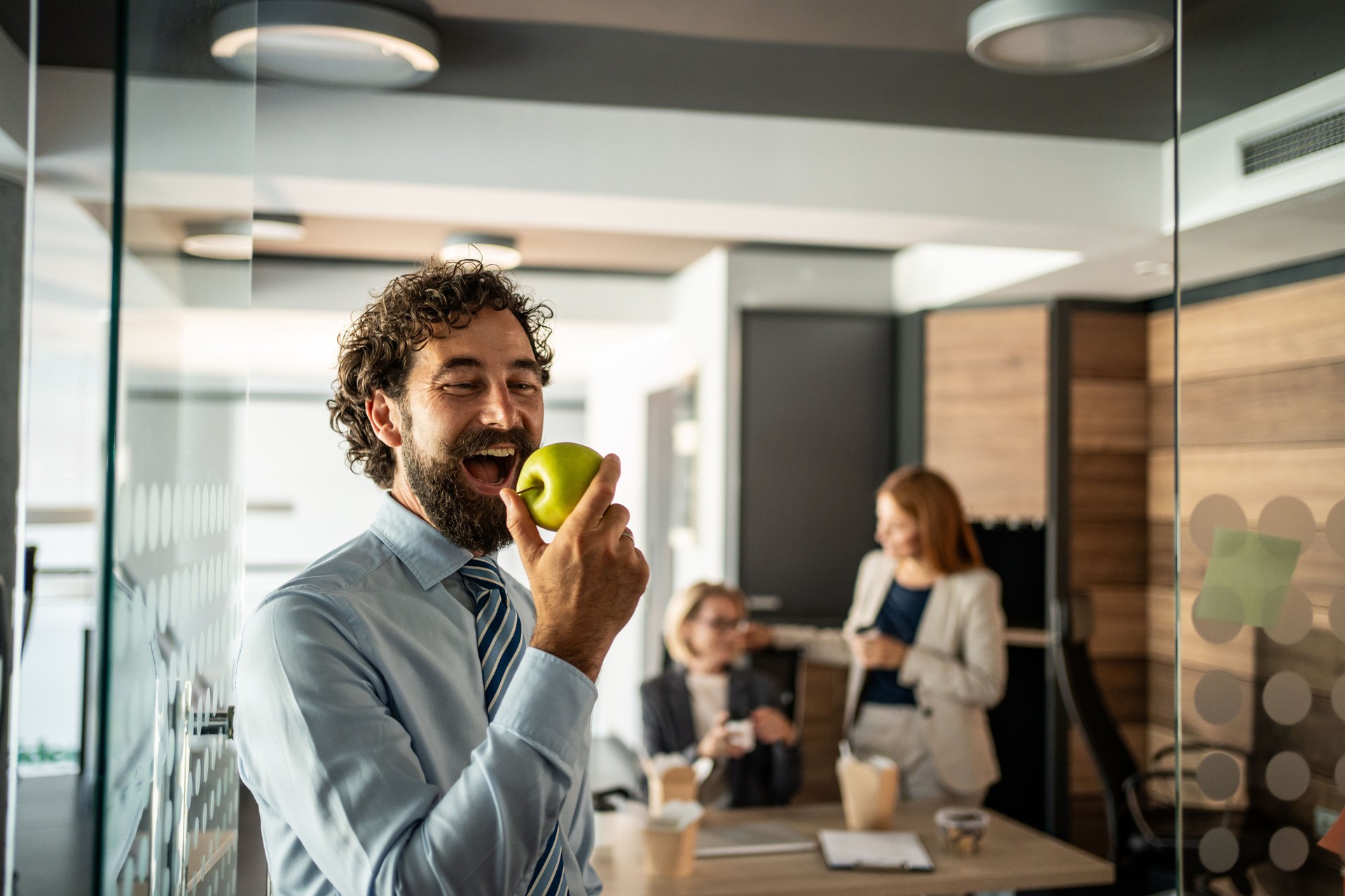 Happy businessman eating green apple in modern office